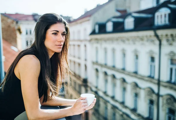 Jovem empresária com xícara de café em pé em um terraço em um escritório na cidade . — Fotografia de Stock