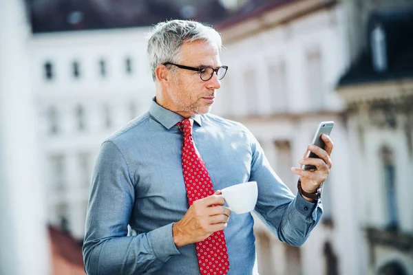 Mature businessman with smartphone standing on a terrace in city, texting. — Stock Photo, Image