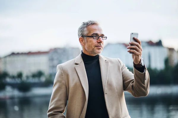 Ώριμες επιχειρηματία με smartphone στέκεται από τον ποταμό στην πόλη Πράγα, λήψη selfie. — Φωτογραφία Αρχείου