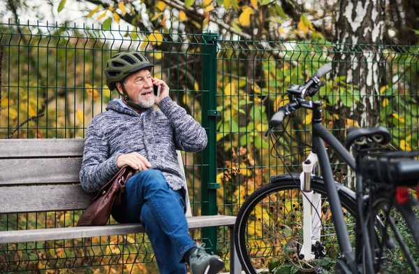 Homme âgé avec électrovélo assis sur un banc à l'extérieur en ville, en utilisant un smartphone . — Photo