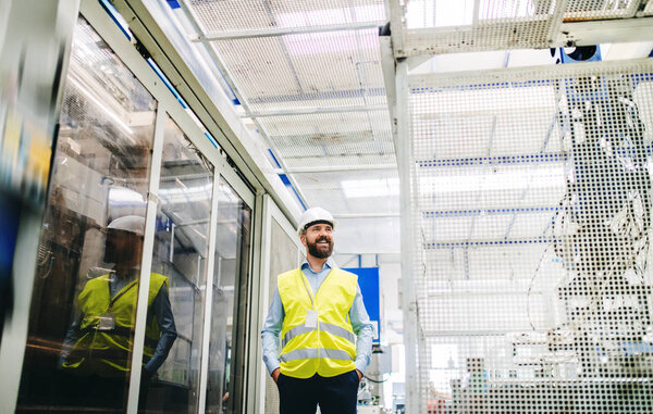 A portrait of an industrial man engineer in a factory, hands in pockets.