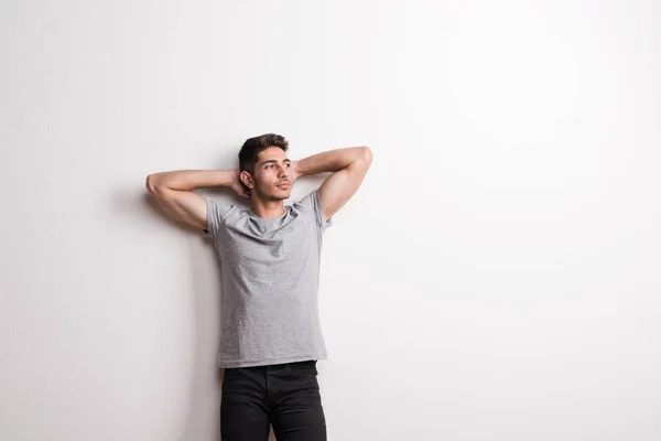 Cheerful young hispanic man standing in a studio, hands behind head. Copy space. — Stock Photo, Image