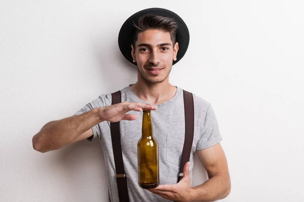 Ein selbstbewusster junger Mann mit Hut in einem Atelier, in der Hand eine leere Bierflasche. — Stockfoto