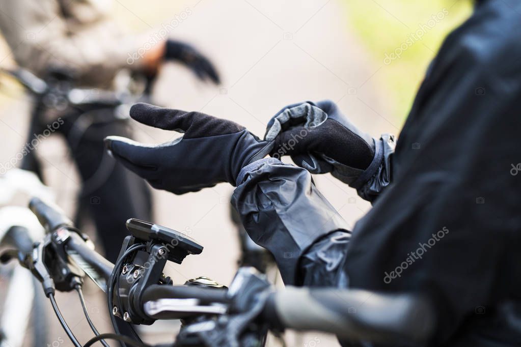 A close-up of a cyclist with electrobike putting on gloves outdoors in park.