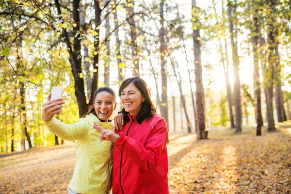 Deux coureuses avec smartphone prenant selfie en plein air dans la forêt en automne nature . — Photo