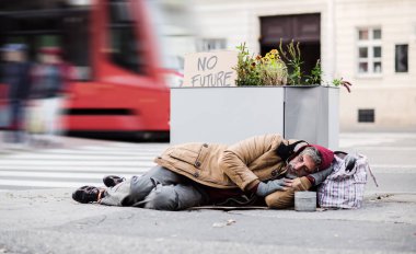 Homeless beggar man lying on the ground outdoors in city asking for money donation. clipart