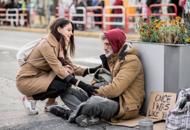 Şehirde oturan evsiz dilenci adam para veren genç kadın.