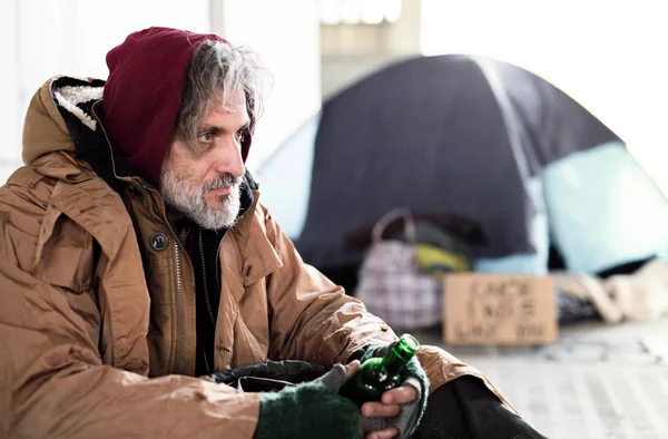 Бездомный нищий сидит на улице, держа в руках бутылку алкоголя. Копирование пространства . — стоковое фото