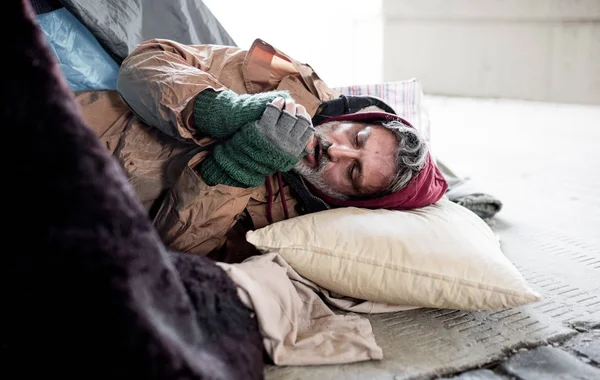 Senzatetto mendicante sdraiato a terra all'aperto in città, scaldandosi le mani . — Foto Stock