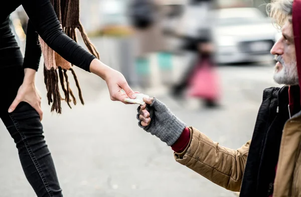 Een buik van vrouw geven van geld aan dakloze bedelaar man zit in de stad. — Stockfoto