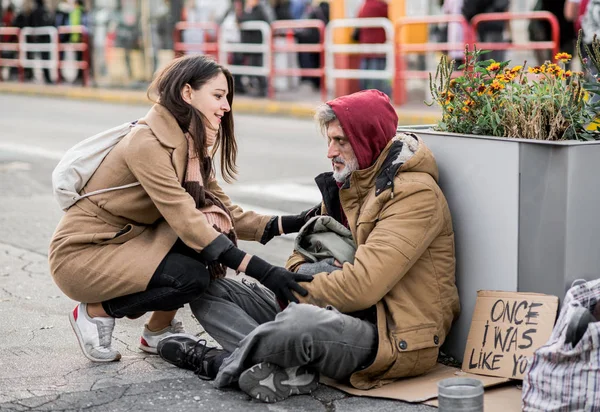 Jonge vrouw geven van geld aan dakloze bedelaar man zit in de stad. — Stockfoto