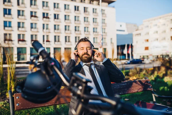 Banlieue homme d'affaires avec vélo assis sur un banc en ville, écouter de la musique . — Photo