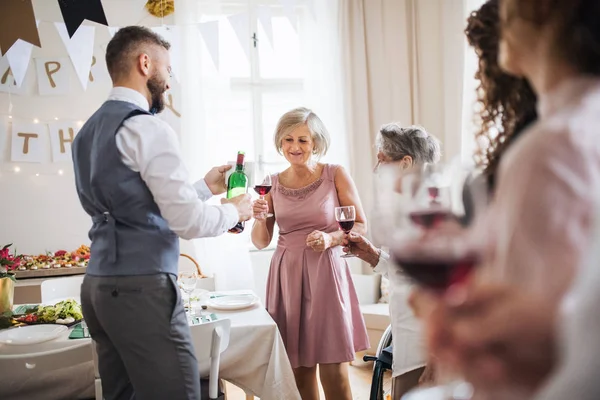 Een man gieten-gasten wijn op een indoor familie verjaardagsfeestje. — Stockfoto