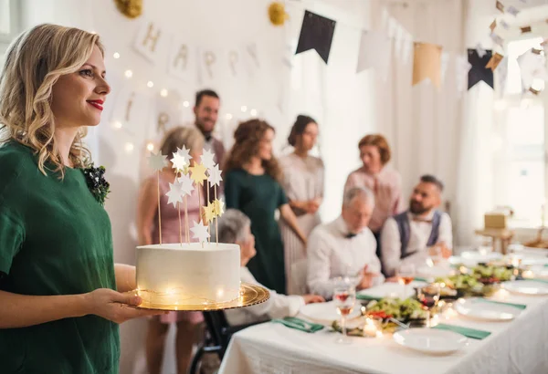 Een jonge vrouw met een cake van de kindverjaardag op een indoor partij. — Stockfoto