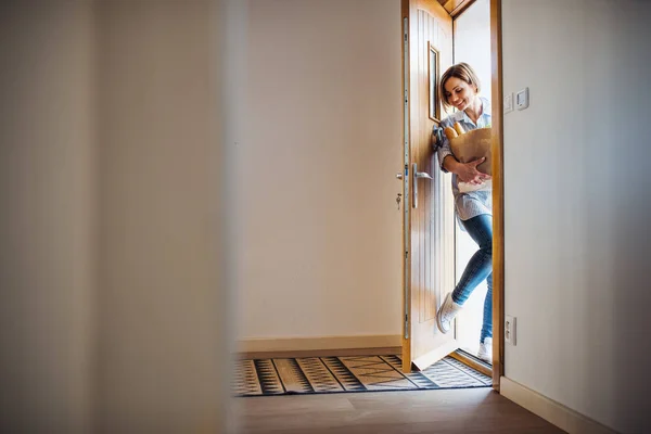 En ung kvinna med matvaror i shopping papperspåse gå i genom ytterdörren. — Stockfoto