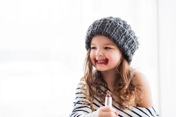 줄무늬 t-셔츠 집에서 작은 행복 한 여자는 립스틱을 적용. — 스톡 사진