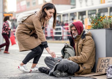 Şehirde oturan evsiz dilenci adam para veren genç kadın.