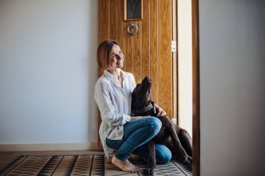 Kapalı yerde evde, bir köpekle oynamayı oturan bir genç kadın.