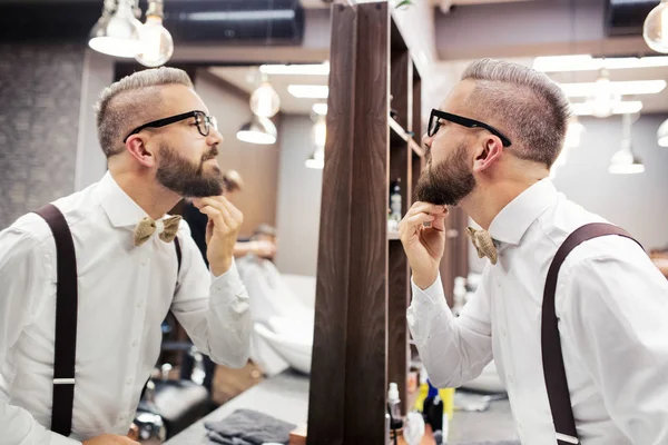 Hipster man klienten med glasögon tittar i spegeln i frisersalong. — Stockfoto