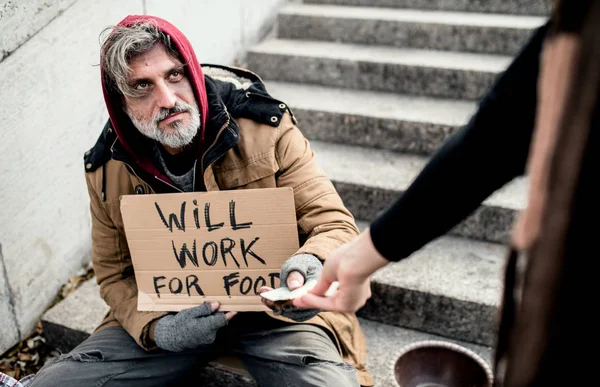 Unerkannte Frau übergibt Geld an obdachlosen Bettler in der Stadt. — Stockfoto