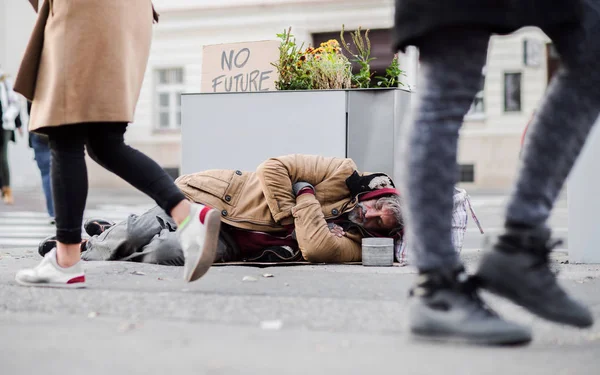 Dakloze bedelaar man liggend op de grond buiten in de stad, slapen. — Stockfoto