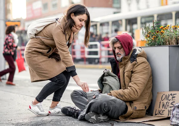 Mujer joven dando dinero a hombre mendigo sin hogar sentado en la ciudad . —  Fotos de Stock