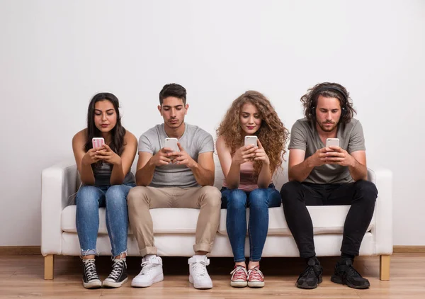 A young group of friends sitting on a sofa in a studio, using smartphones.