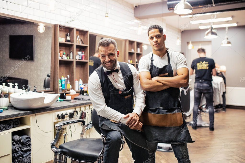 Two male haidressers and hairstylists sitting in barber shop.