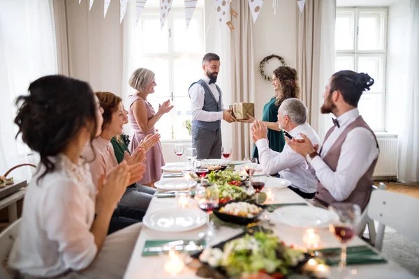 Un homme offrant un cadeau à une jeune femme surprise lors d'une fête d'anniversaire de famille . — Photo