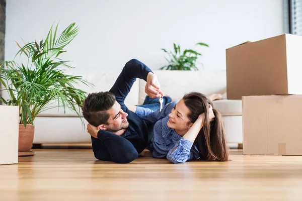 Um jovem casal com uma chave e caixas de papelão se movendo em uma nova casa . — Fotografia de Stock