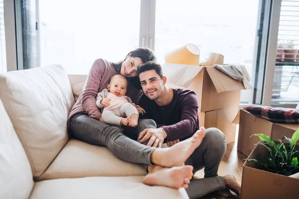 Um retrato de um jovem casal com um bebê e caixas de papelão se movendo em uma nova casa . — Fotografia de Stock