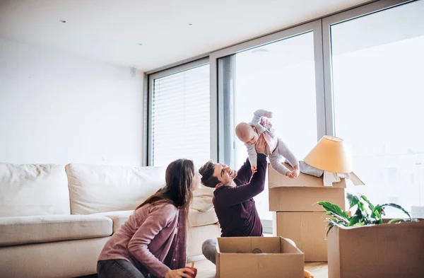 Casal jovem com um bebê e caixas de papelão se movendo em uma nova casa . — Fotografia de Stock