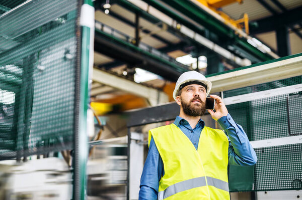 A portrait of an industrial man engineer with smartphone in a factory, working.