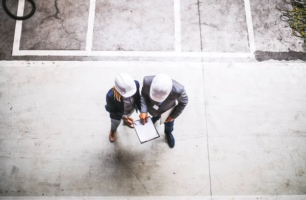 Yukarıdan bir fabrika içinde clipboard ile endüstriyel bir erkek ve kadın mühendis. — Stok fotoğraf