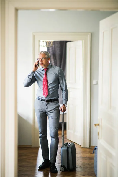 Зрелый бизнесмен в командировке, стоящий в гостиничном номере, используя смартфон . — стоковое фото