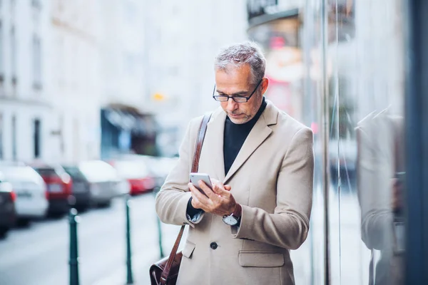 Homme d'affaires mature debout dans une rue de la ville, tenant smartphone . — Photo
