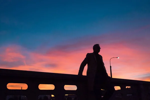 Una silueta de hombre de negocios de pie en un puente al atardecer . — Foto de Stock