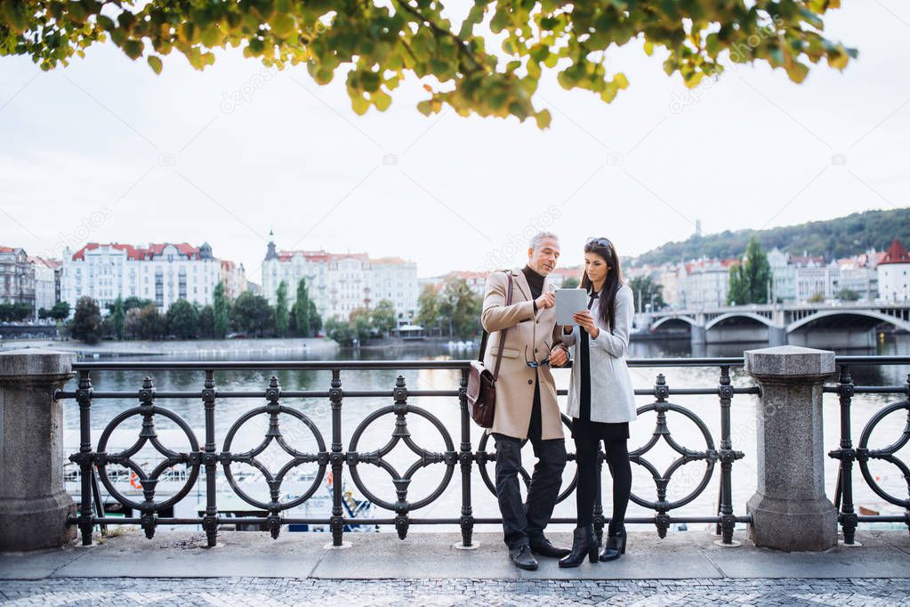 Man and woman business partners with tablet standing by a river in city of Prague.