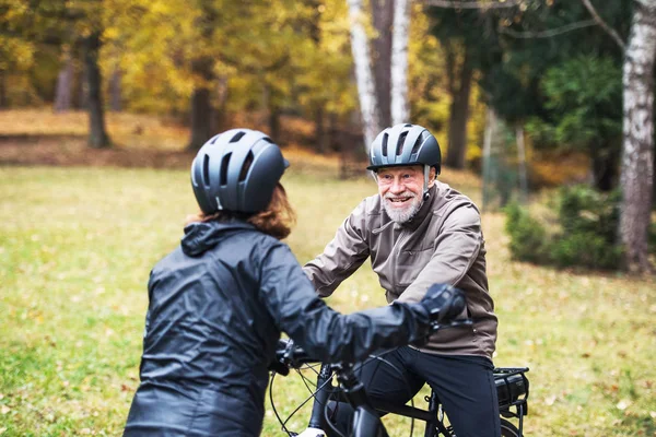 Aktywny senior para z electrobikes stojący na zewnątrz na drodze w przyrodzie. — Zdjęcie stockowe