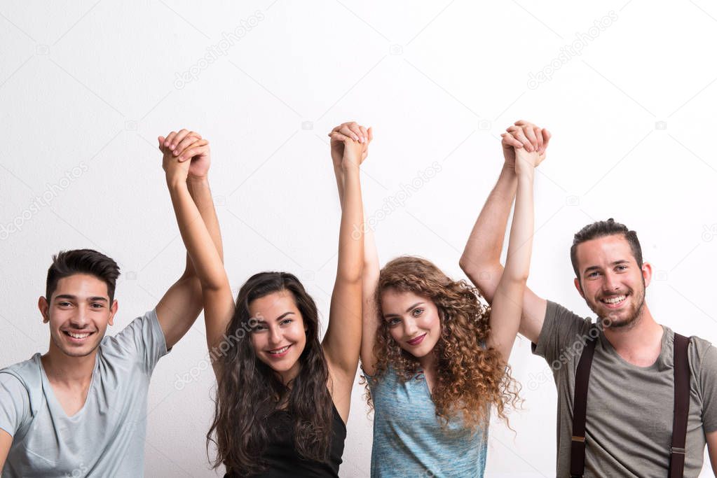 Joyful young group of friends standing in a studio, lifting hands.