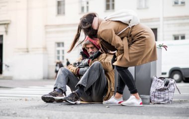 Şehirde oturan evsiz dilenci adam para veren genç kadın.
