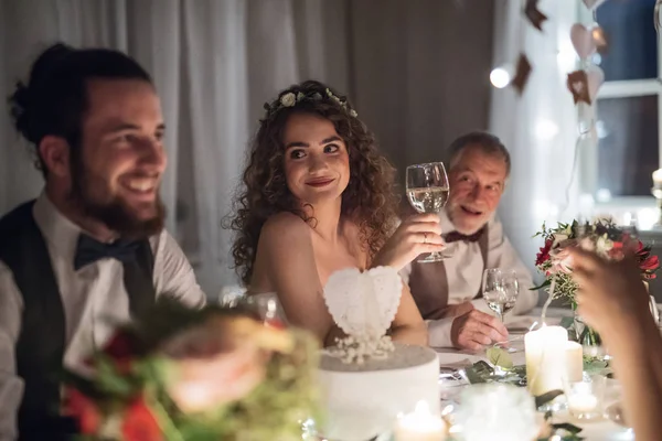 Ett ungt par som sitter vid ett bord på ett bröllop, pratar med gäster. — Stockfoto