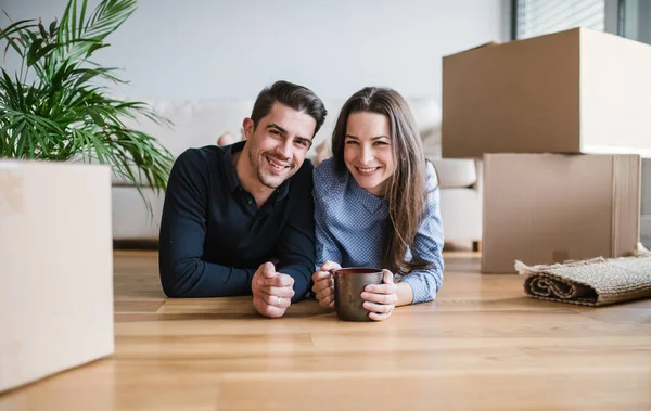 Un jeune couple avec une tasse et des boîtes en carton se déplaçant dans une nouvelle maison . — Photo