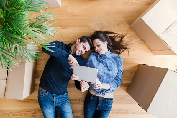 Вид сверху на молодую пару с планшетом и картонными коробками, переезжающую в новый дом . — стоковое фото