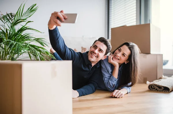 A young couple with a smartphone moving in a new home, taking selfie. — Stock Photo, Image