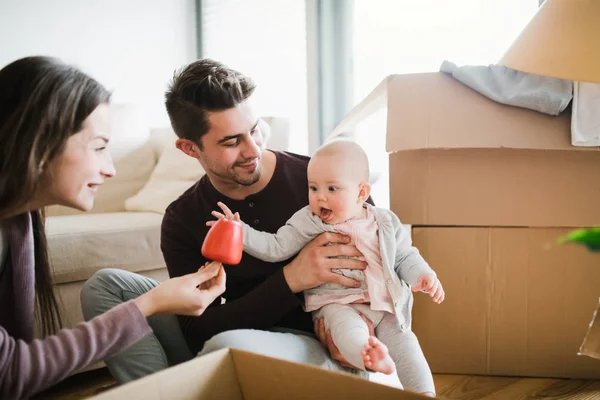 Unga par med en bebis och pappkartonger som rör sig i ett nytt hem. — Stockfoto