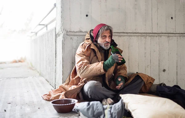Una vista frontale di un mendicante senzatetto seduto all'aperto, con in mano una bottiglia di alcol. Copia spazio . — Foto Stock