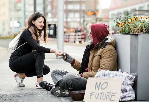 Jeune femme donnant de l'argent à un mendiant sans abri assis en ville . — Photo