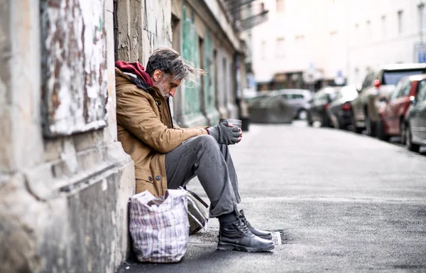 Hombre mendigo sin hogar sentado al aire libre en la ciudad pidiendo una donación de dinero . — Foto de Stock