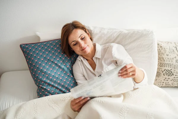 朝の寝室のベッドで新聞を読む若い女性. — ストック写真